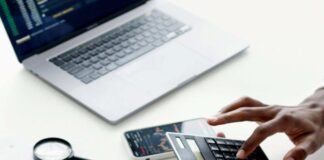 osoba unosi brojeve na digitronu, sa laptopom i telefonom sa dijagramima ispred na stolu